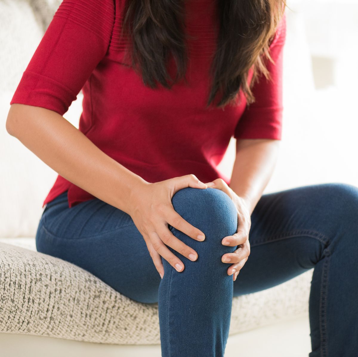 Midsection Of Woman Touching Knee In Pain While Sitting At Home