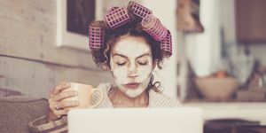 Woman Wearing Hair Curlers And Face Mask While Using Laptop At Home