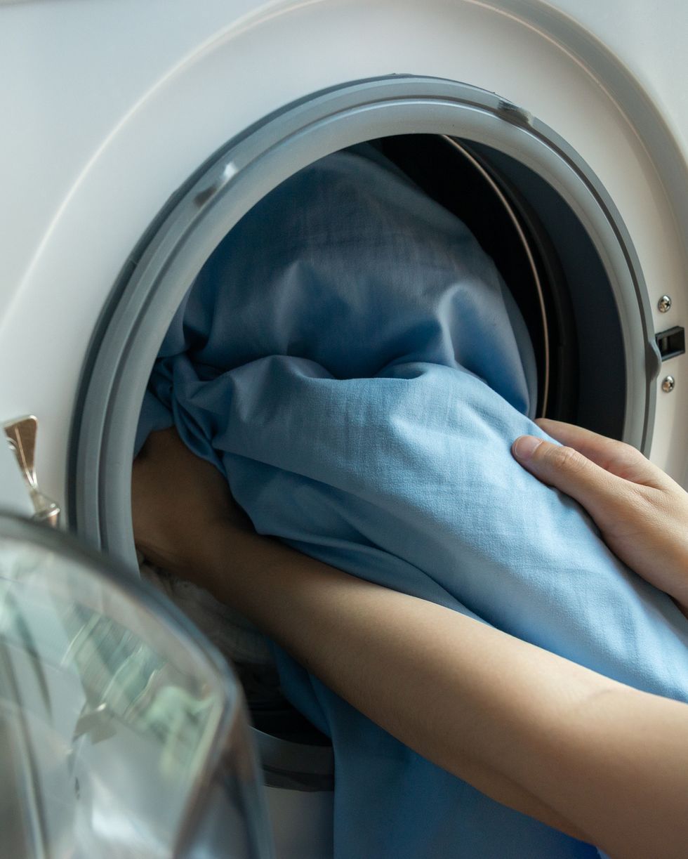 woman’s hand loading dirty blue bed sheets in a white washing machine