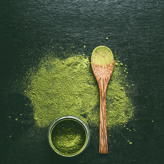 matcha japanese green tea powder with wooden spoon on dark background, top view