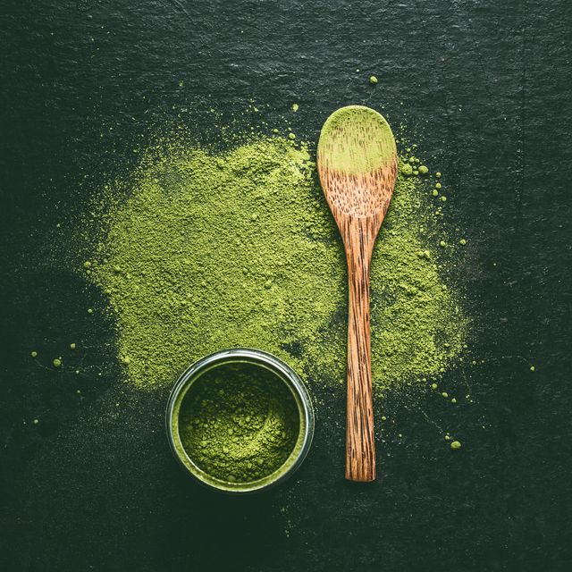 matcha japanese green tea powder with wooden spoon on dark background, top view