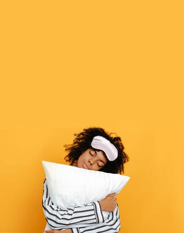 sleeping. dreams. woman portrait. afro american girl in pajama is hugging a pillow, on a yellow background