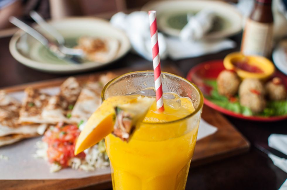 a close up view of pineapple mango shake with striped paper straw on a dining table with mexican dishes