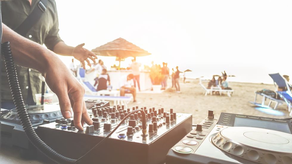 dj mixing at sunset beach party in summer vacation outdoor   disc jockey hands playing music for tourist people in chiringuito kiosk bar   event, music and fun concept   focus on right hand