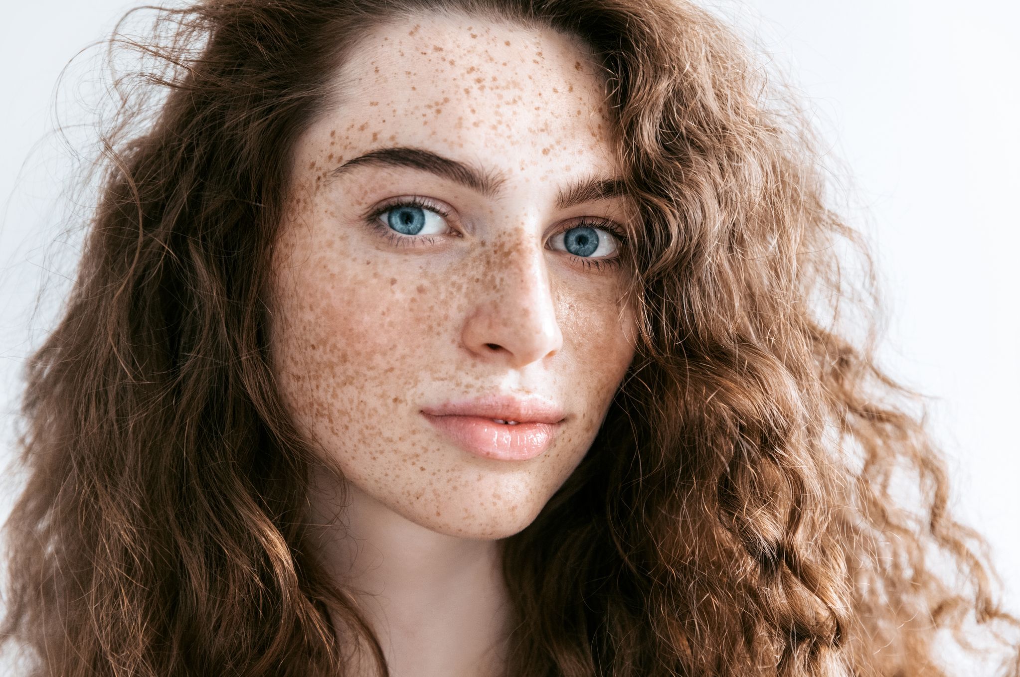 Beautiful Freckles young woman close up portrait. Attractive model with beautiful blue eyes and ginger curly hair