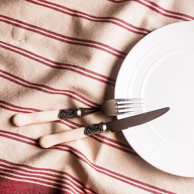 empty white plate, fork and knife on a red and white linen striped napkin, top view image with copy space kitchen table with a towel and a plate   top view with copy space