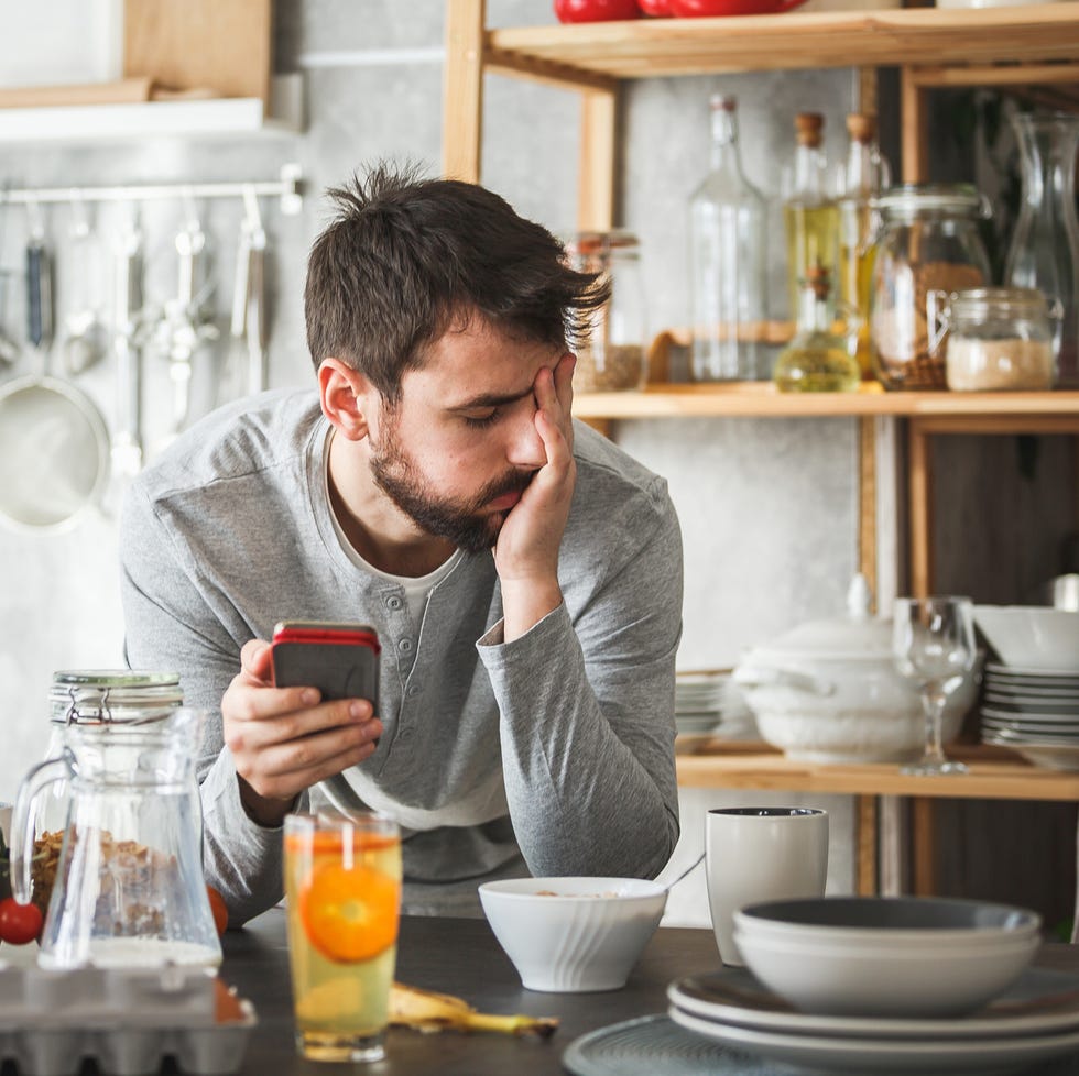 Sad man using smart phone during breakfast at home