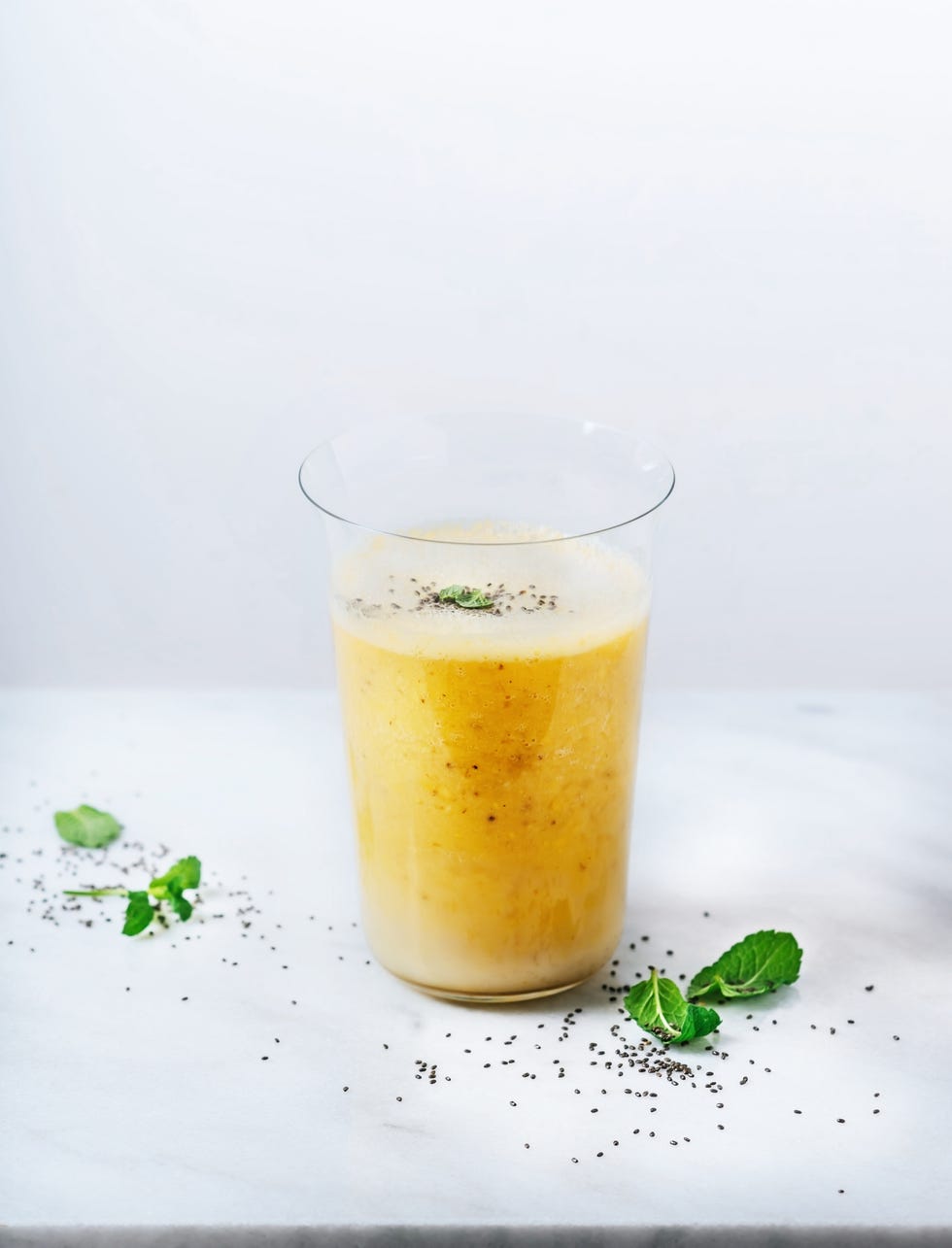 a glass of banana and mango smoothie with mint garnish on white background with chia seeds