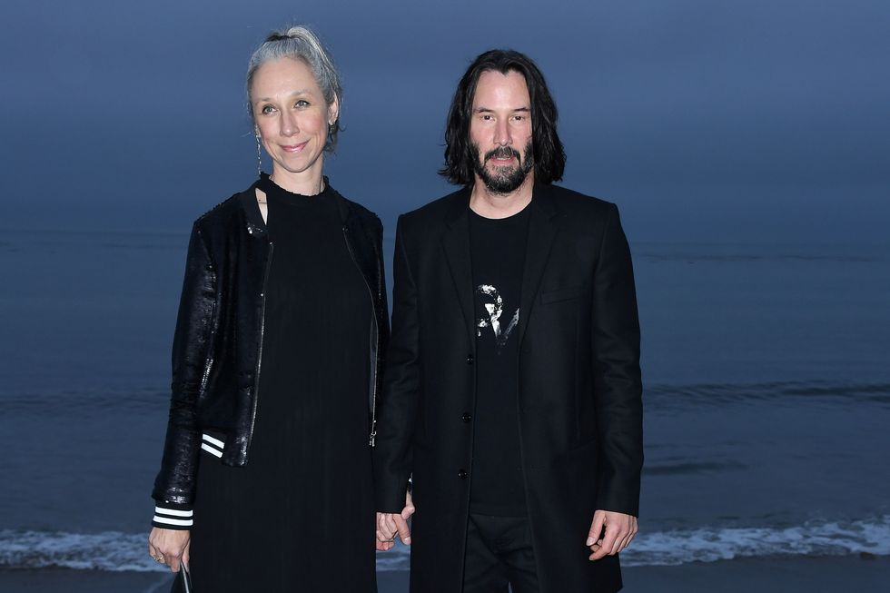 Keanu Reeves and Alexandra Grant hold hands on the beach, posing for cameras.