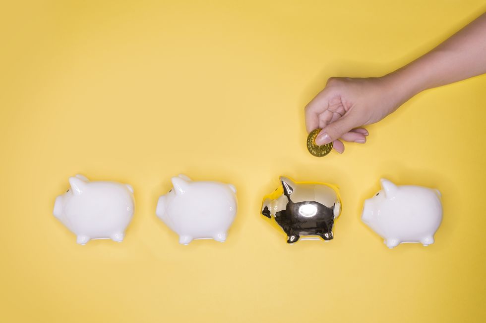 hand putting coin into a golden piggy bank from a group of white piggy bank