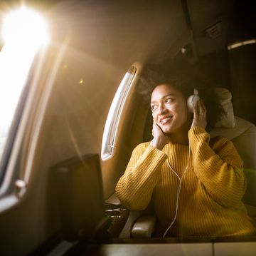 young fashionable woman sitting on a private airplane and looking through a window while listening to music through headphones