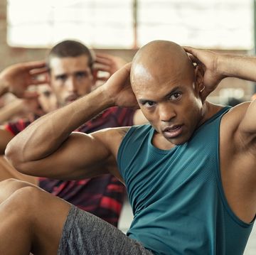 muscular african american man doing sit ups at gym with other people in background mature black man doing abs workout with class at cross training gym muscular guy doing crunches