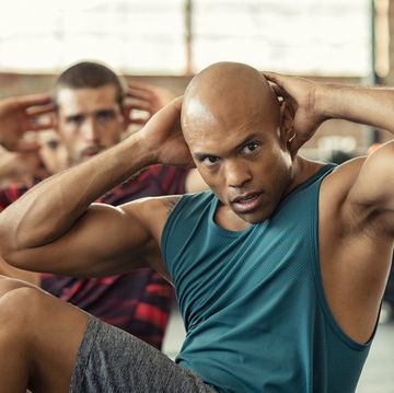 muscular african american man doing sit ups at gym with other people in background mature black man doing abs workout with class at cross training gym muscular guy doing crunches