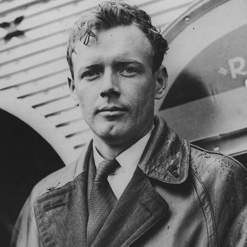 charles lindbergh looks at the camera, he wears a leather jacket, collared shirt and tie
