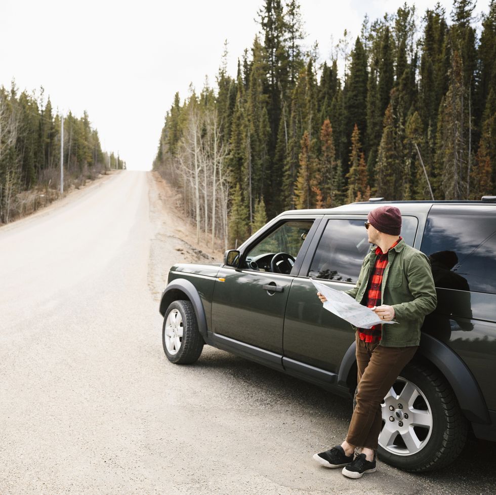 Man with map standing outside SUV at remote roadside