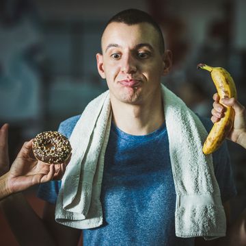uncertain male athlete choosing between donut and banana in a gym