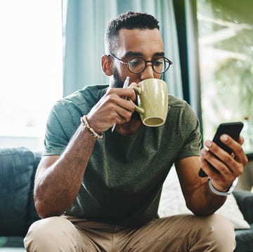 What's the vibe on the newsfeed shot of a young man using a smartphone and having coffee on the sofa at home