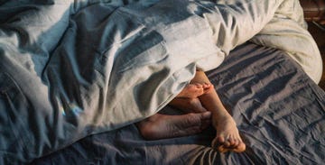 Two pairs of feet partially covered by a blanket on a bed