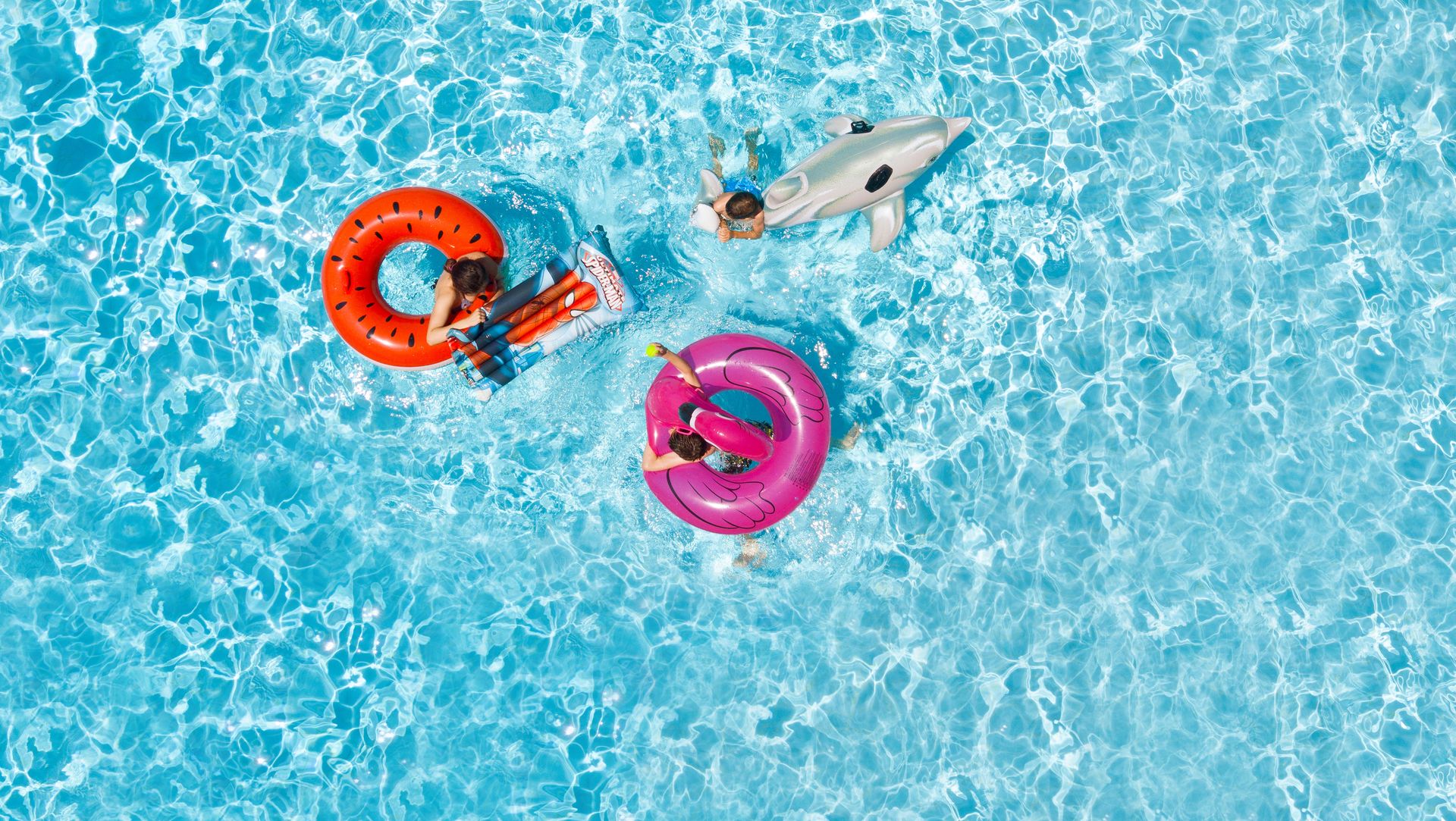 Three childred on inflatable floats in swimming pool