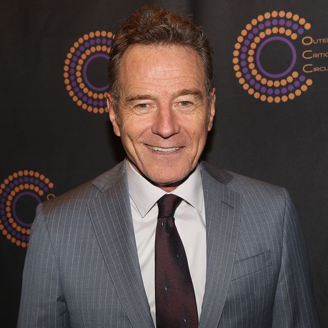 bryan cranston smiles at the camera, he wears a gray pinstriped suit jacket, light collared shirt and maroon tie