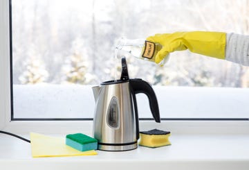 woman pouring natural destilled acid white vinegar in electric kettle to remove boil away the limescale descaling a kettle, remove scale concept