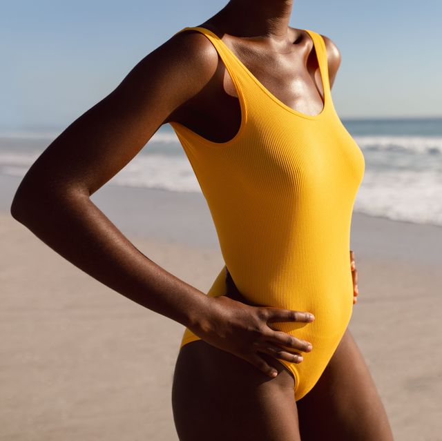 mid section of african american woman in swimwear standing with hands on hip on the beach