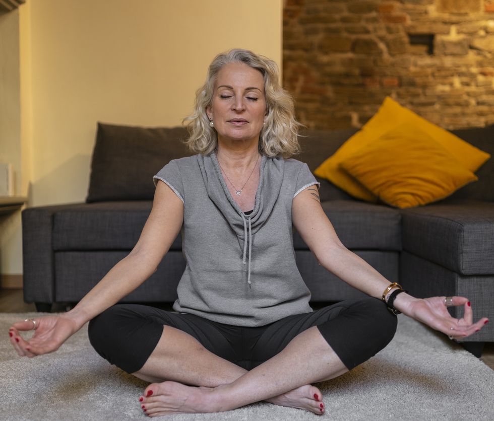 portrait of mature woman sitting on carpet in the living room meditating
