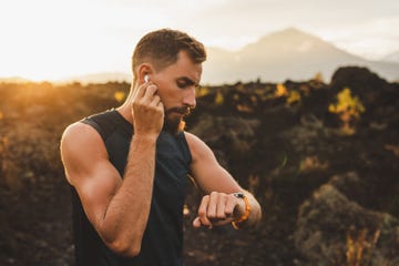 male runner synchronizing wireless earphones with smart watch preparing for trail running outdoors at sunrise