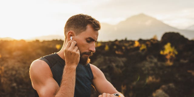 Male runner synchronizing wireless earphones with smart watch. Preparing for trail running outdoors at sunrise. male runner synchronizing wireless earphones with smart watch preparing for trail running outdoors at sunrise
