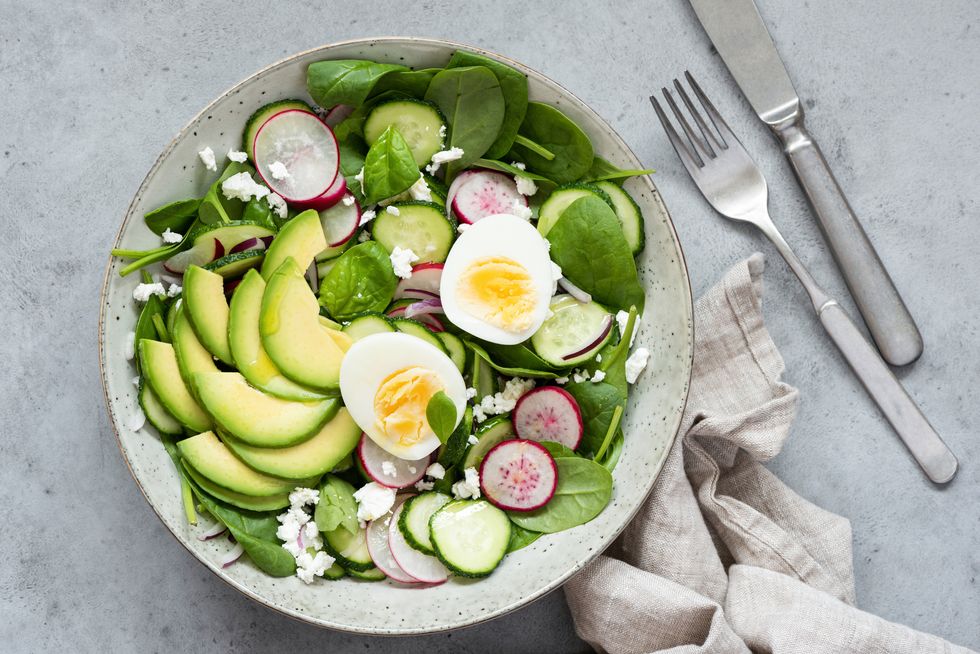 healthy salad bowl with avocado, baby spinach, cucumber, radish and boiled egg table top view, concrete background