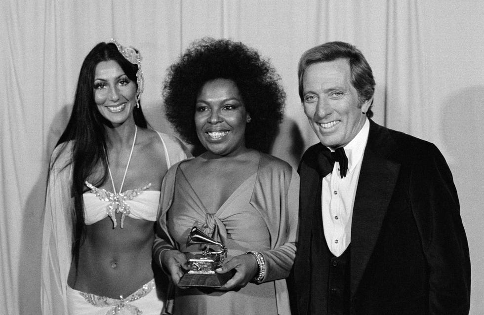 three individuals posing together with one holding a grammy award