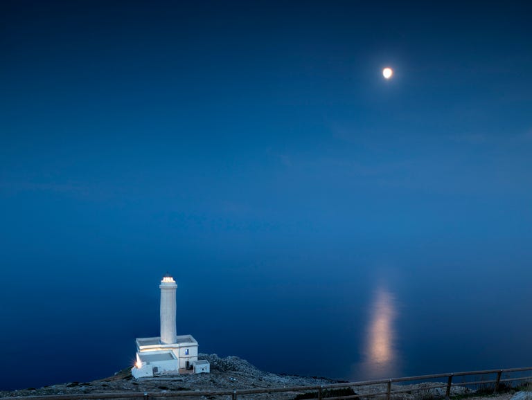 blue dusk and moon reflected in the sea frames the lighthouse at punta palascia, otranto, province of lecce, apulia, italy