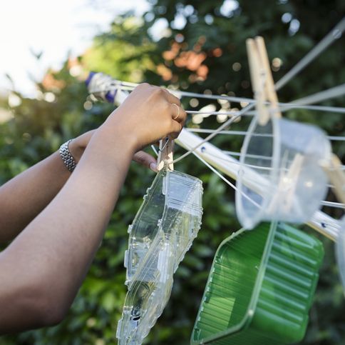 young woman hanging washed plastic containers onto a clothesline to dry