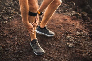 hardloper grijpt naar scheenbeen vanwege shinsplints, op gravel ondergrond