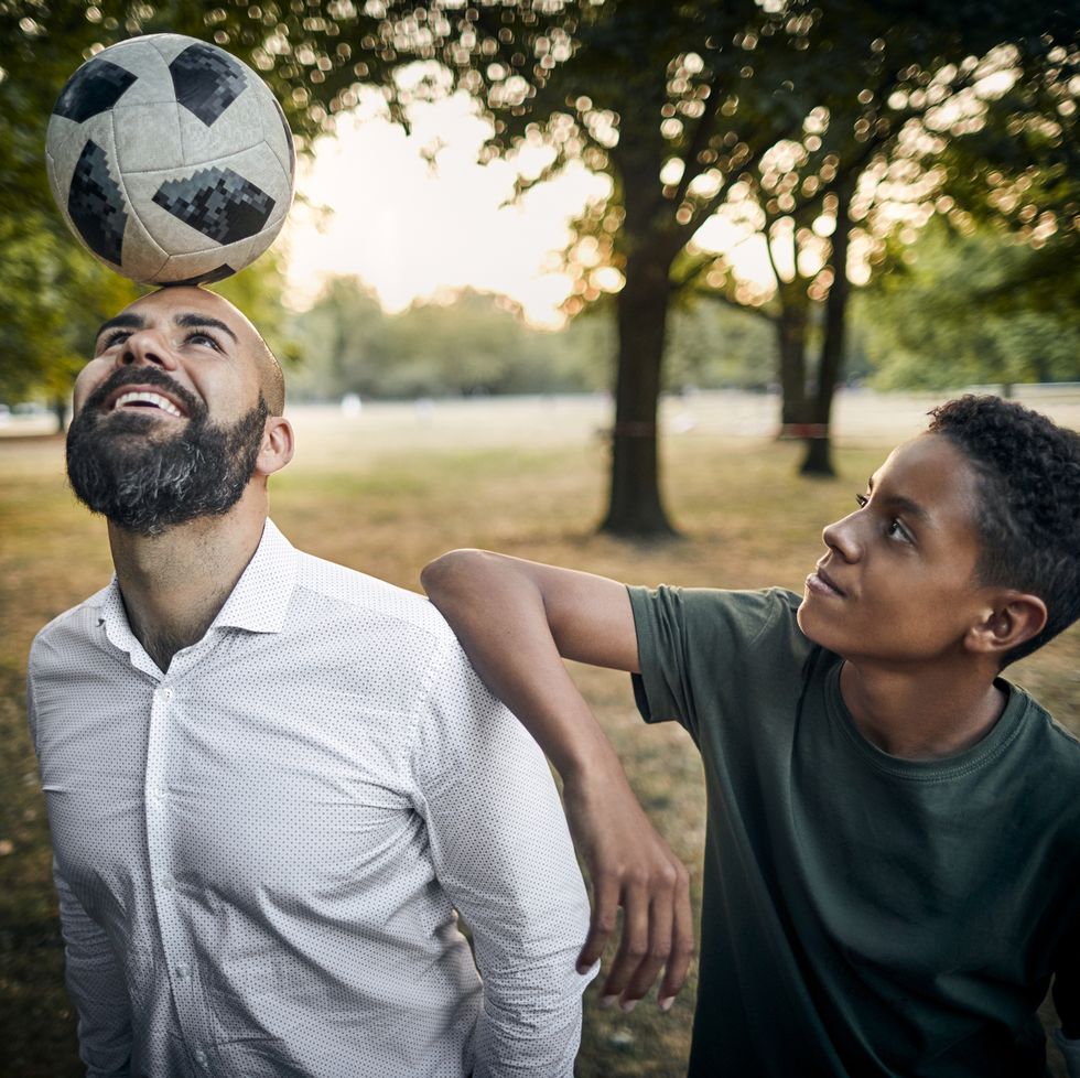 Teenage boy looking at father balancing a soccer ball on his head in a park