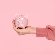 hand of female holding piggy bank while holding it on pink background