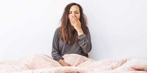 girl under bedsheets yawning from fatigue