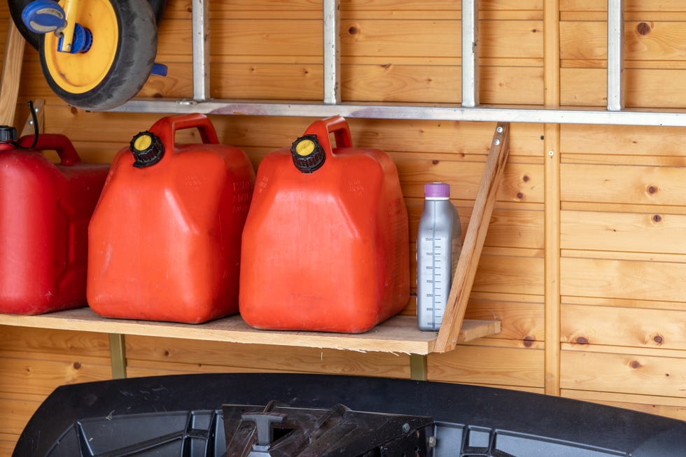 garage corner with three red plastic fuel cans , staircase and snow plough for atv with wooden wall on background. petrol gas containers reserves storage at vehicle home garage.