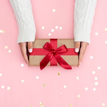 Womans hands holding gift or present box decorated confetti on pink pastel table top view. Flat lay composition for birthday or wedding.