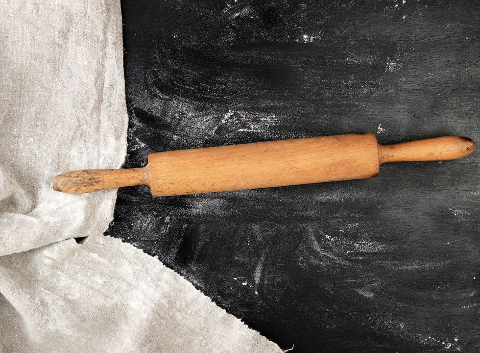 wooden rolling pin on a black background, white wheat flour, top view, copy space
