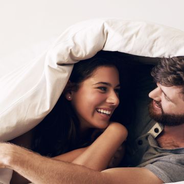shot of a happy young couple covering themselves with a blanket on the bed at home