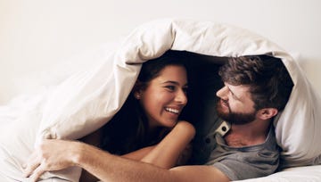 shot of a happy young couple covering themselves with a blanket on the bed at home