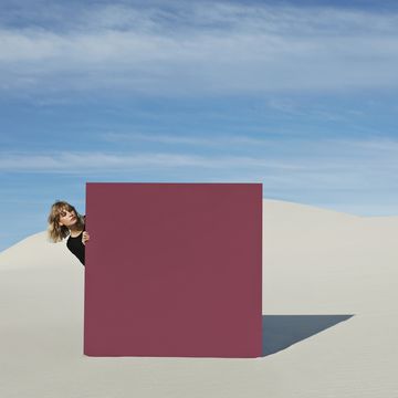 Young woman peeking through maroon portal at desert against sky
