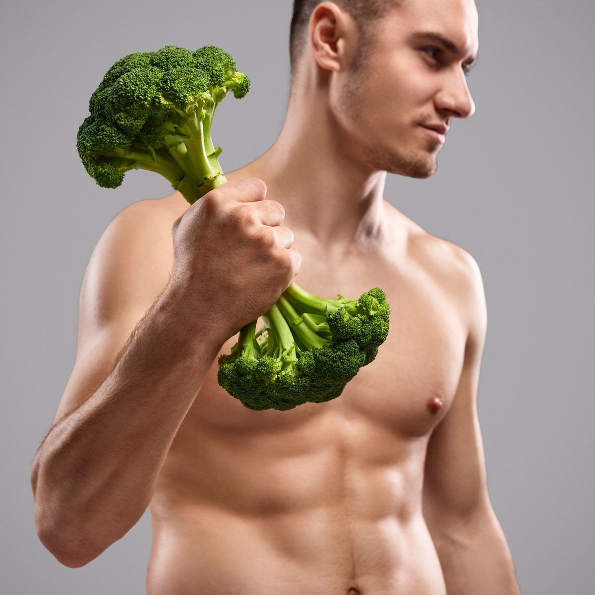 Shirtless man exercising with broccoli