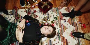 Laughing woman lying on floor covered in bows and confetti during holiday party with friends