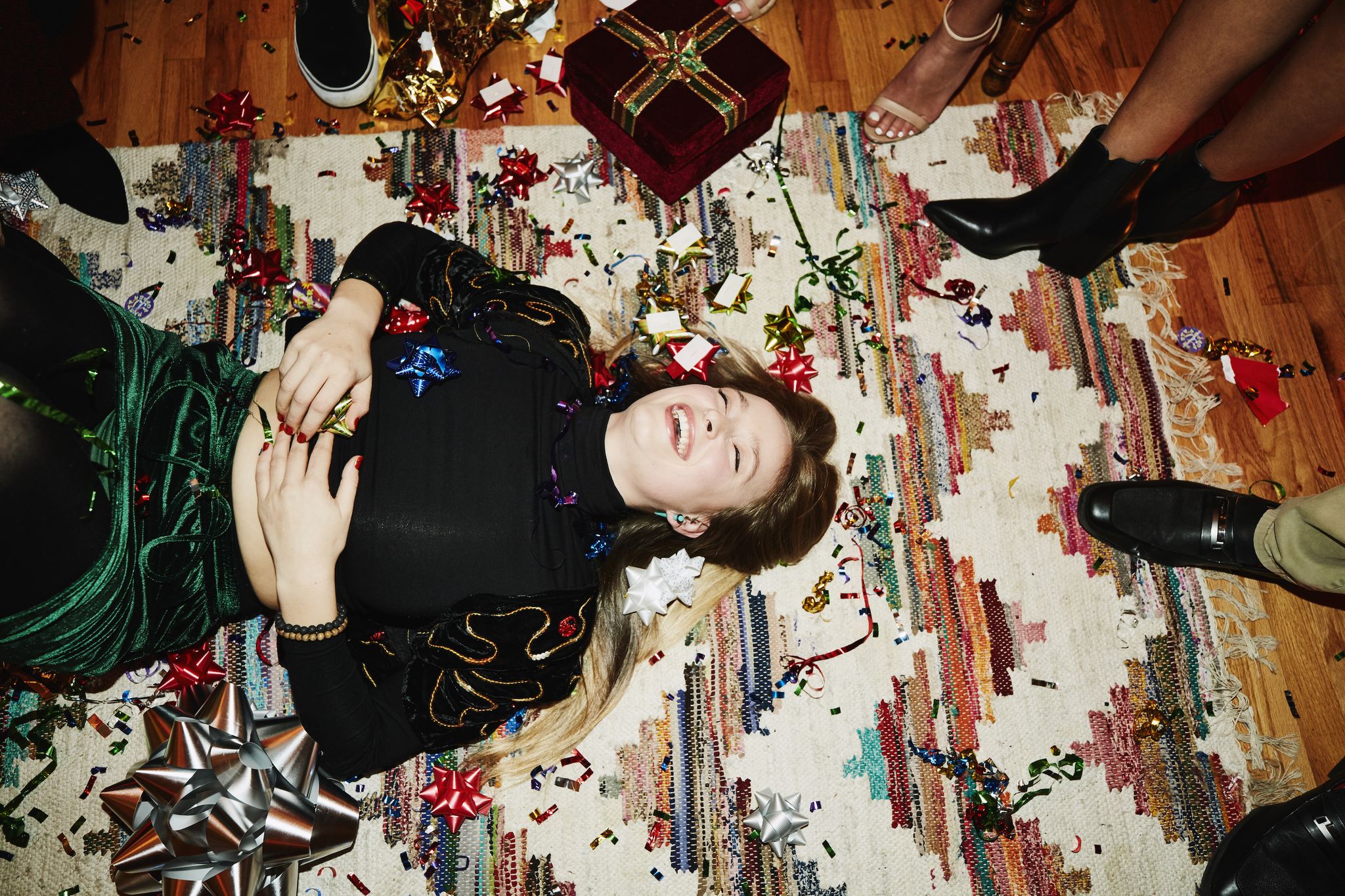 Laughing woman lying on floor covered in bows and confetti during holiday party with friends