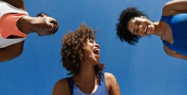 directly below shot of cheerful female sportspeople against blue sky during sunny day