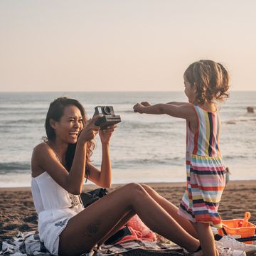 two people, mother and daughter relaxing on the beach, mother is taking pictures with instant camera