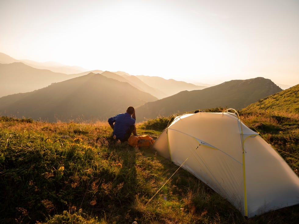 male hiker in rear view resting in the mountain around his tent and looking the sunset, live in adventure