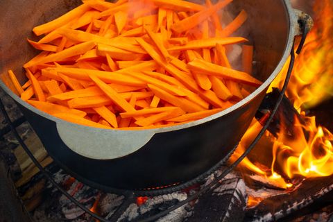 Open air kitchen at party picnic. Pilaf cooking on fire outdoor. Big pot with sliced carrot stays on wire rack and steams. Close up image of meal dish preparation